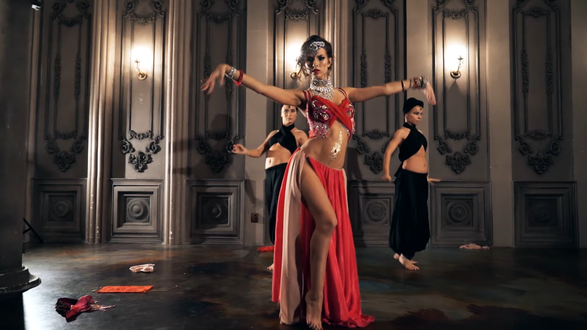 Beautiful woman in a red oriental dress dancing in a dark room with two other women in the background