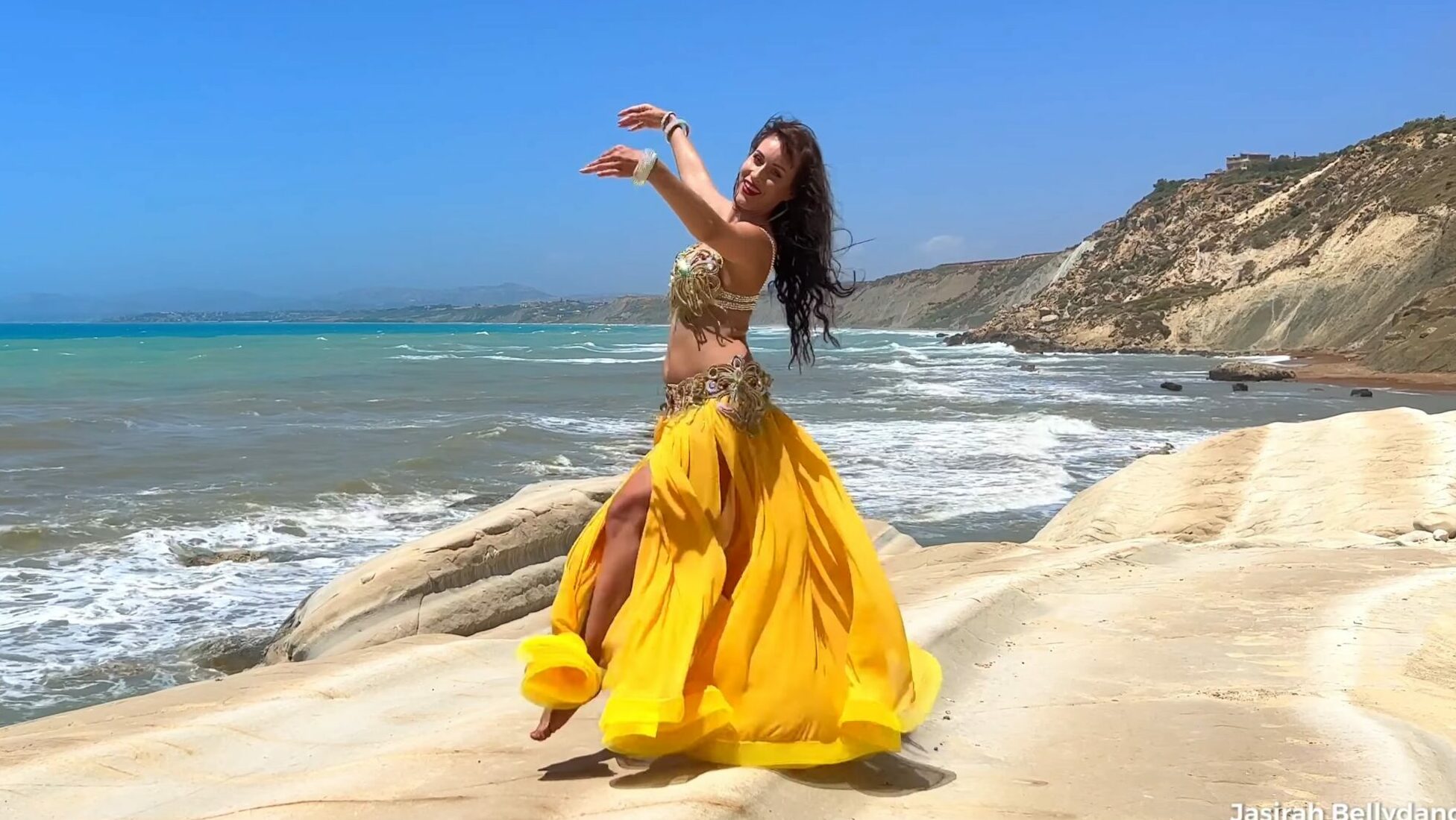 Woman in yellow skirt belly dancing near the sea