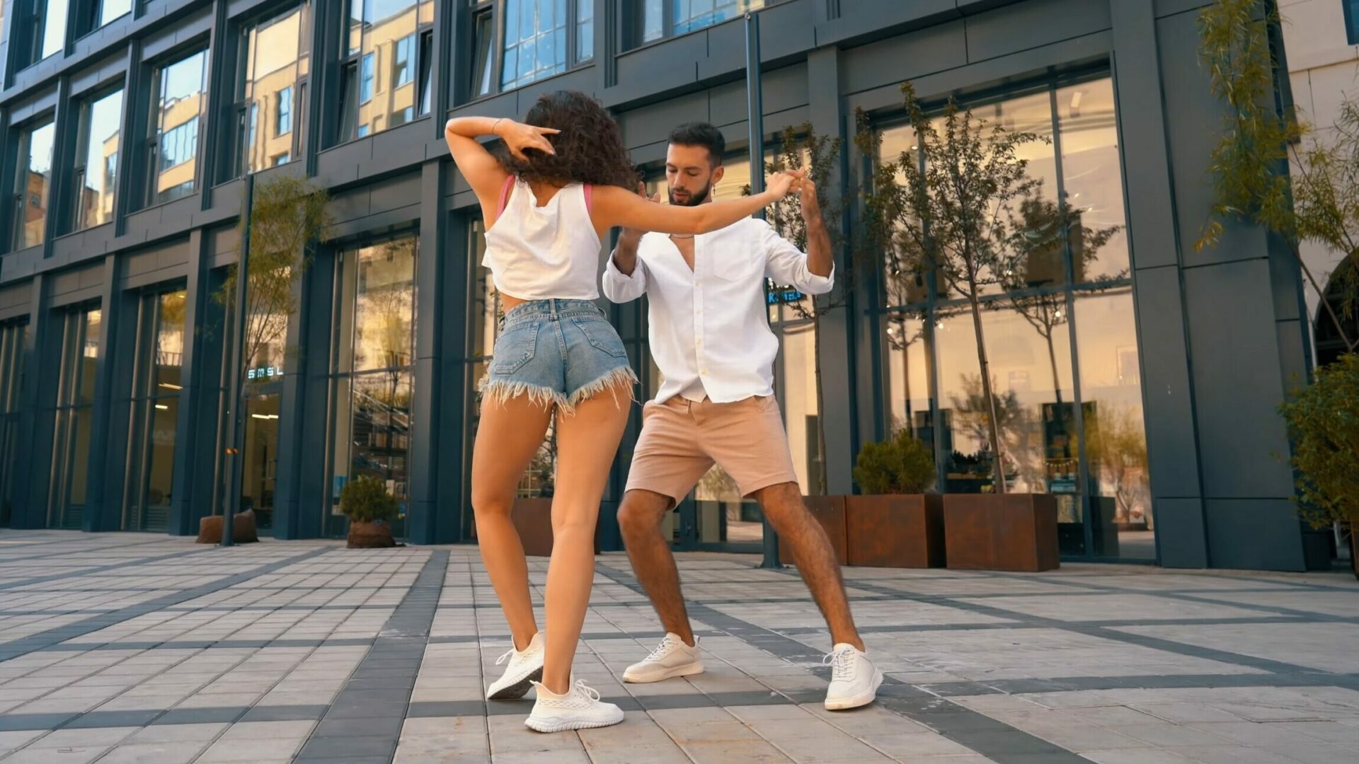 Woman in blue shorts and white top dancing bachata on the street with a man in beige shorts and white shirt