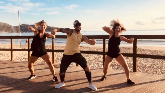 A man and two women dancing zumba on the beach