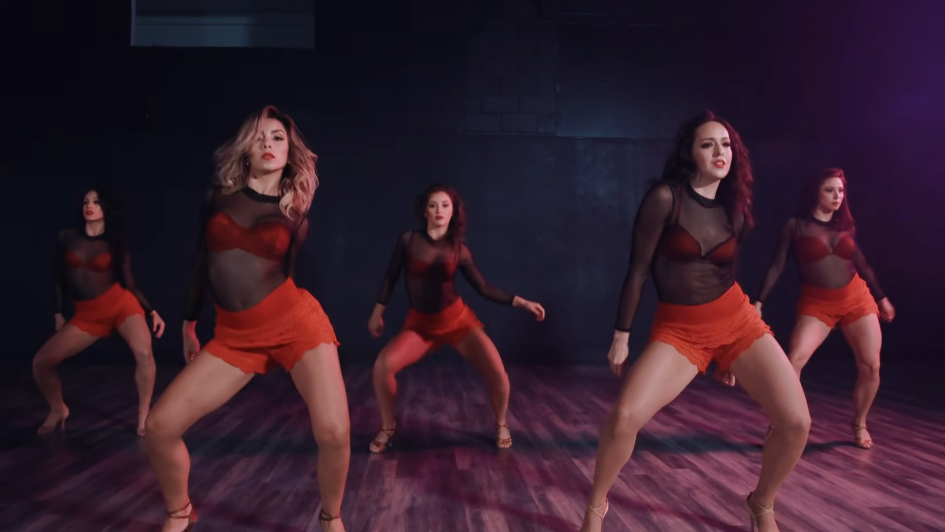 Five women in red short shorts and see through top dancing on stage