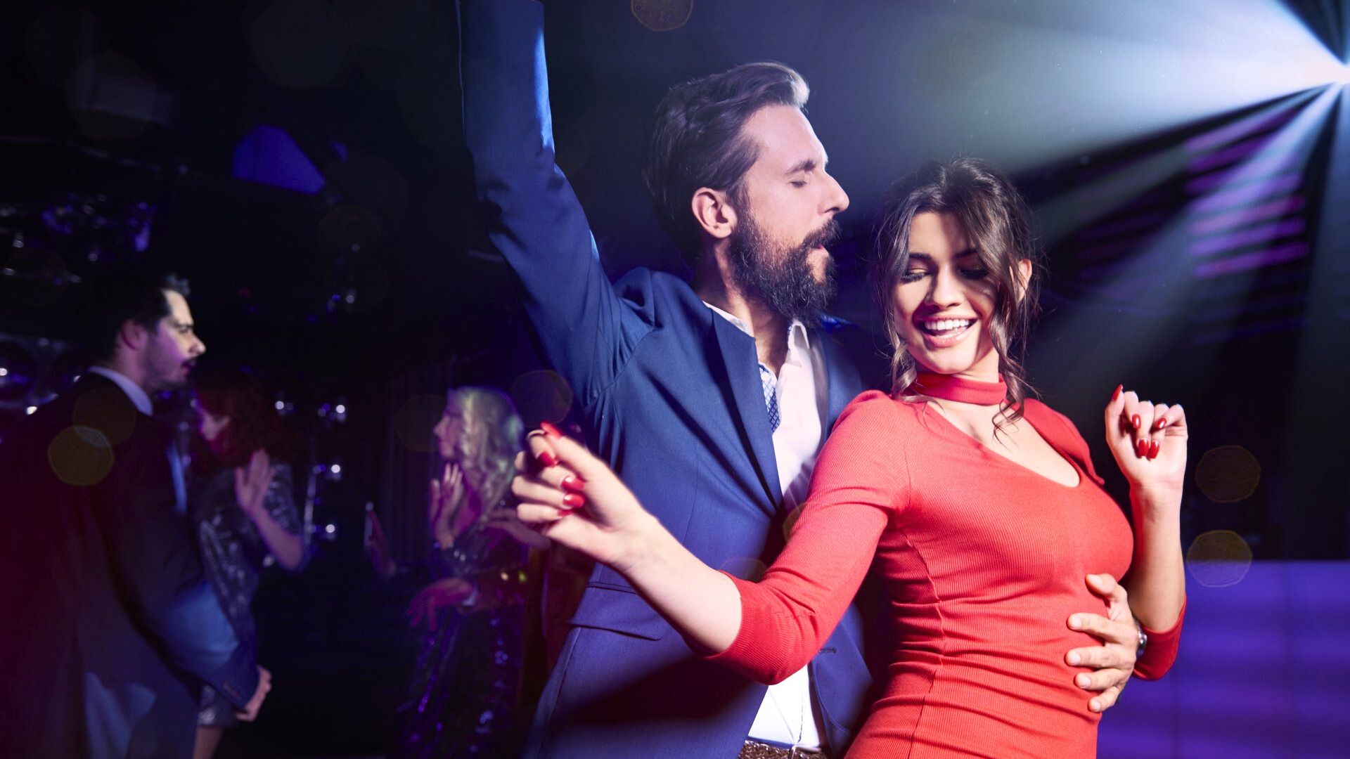A man in suite dancing with a woman in red dress at a party in a night club