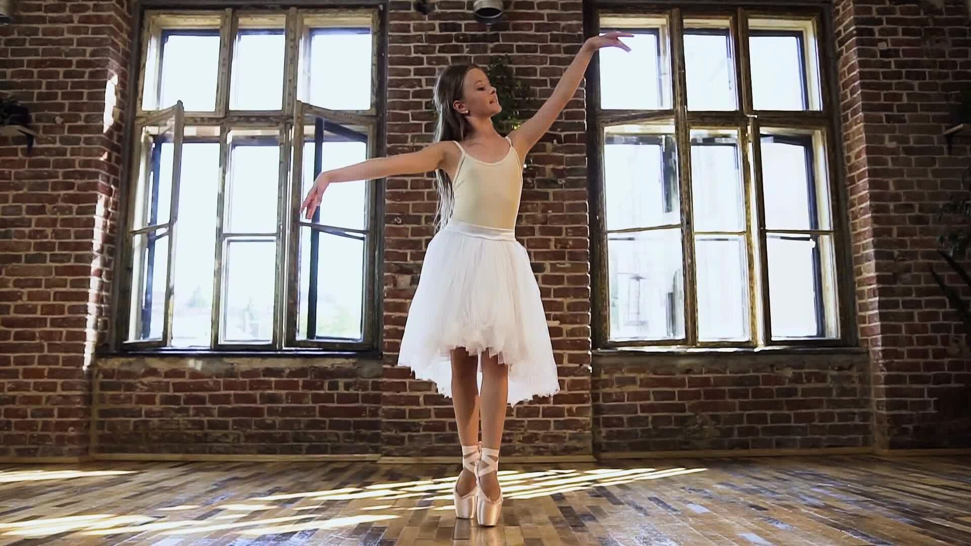 A girl in white tutu dress dancing ballet in front of the windows