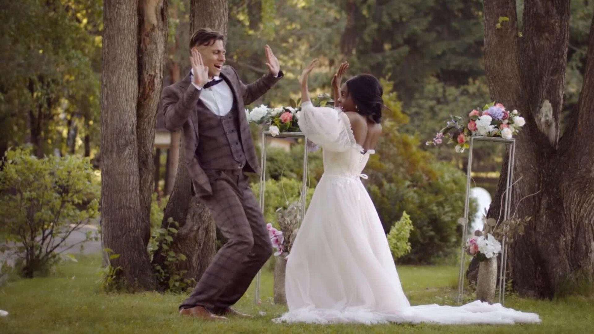 Young newlyweds dancing outside with their hands raised